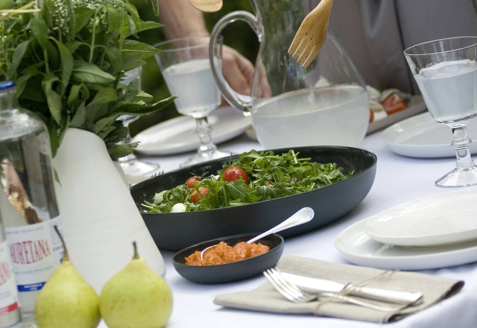 Table dressée en plein air, avec salade, carafes et poires